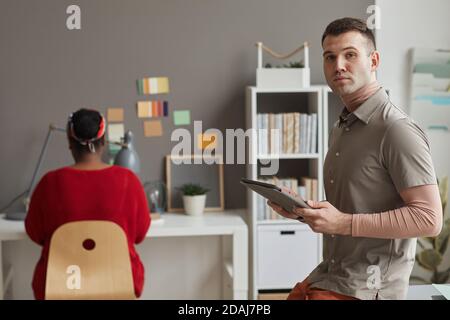 Portrait of young designer looking at camera while using digital tablet at office with businesswoman working at the table in the background Stock Photo