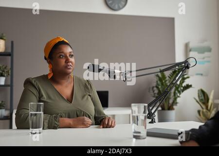 African overweight woman sitting at the table and speaking on microphone giving an interview on radio Stock Photo