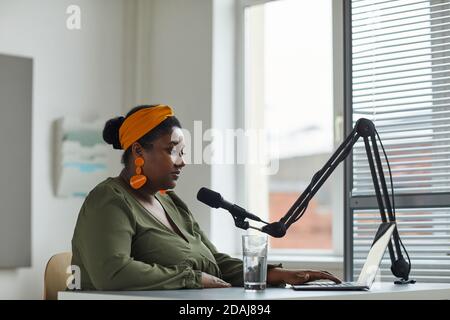 African radio host sitting at the table in front of laptop and speaking on microphone working on radio Stock Photo