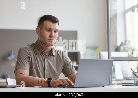 Young man sitting at his workplace and typing on laptop he working online at office Stock Photo