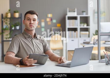 Portrait of young graphic designer sitting at the table looking at camera he using digital tablet and laptop in his work Stock Photo