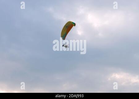 A tandem motor paraglider flies through the evening cloudy sky with a pilot and a passenger. Stock Photo