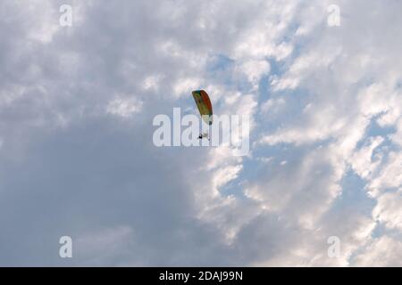 Tandem motor paraglider flies through a beautiful evening cloudy sky with a pilot and a passenger. Stock Photo