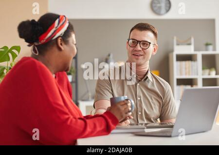 Two young colleagues sitting at the table and working on laptop together in team during meeting at office Stock Photo