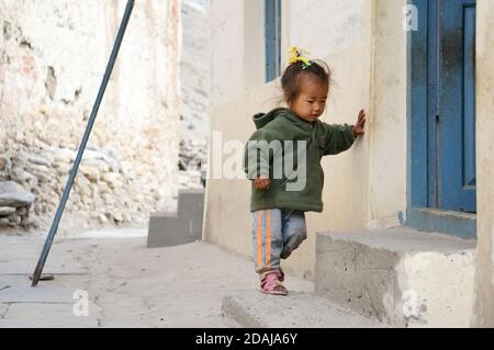 A little Nepalese girl walks near a residential stone house on a settlement street. Hike in the closed area of the upper Mustang. Nepal. Stock Photo