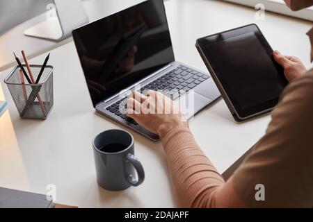 Close-up of man sitting at the table typing on laptop and connecting tablet pc with computer Stock Photo
