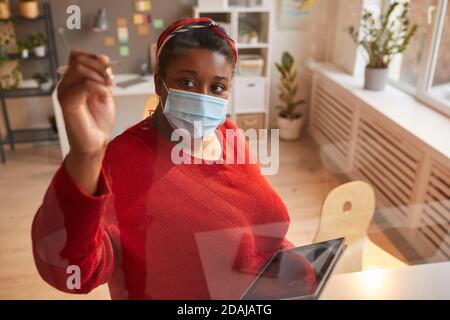 African woman in protective mask writing on the wall and using tablet pc she working at office Stock Photo
