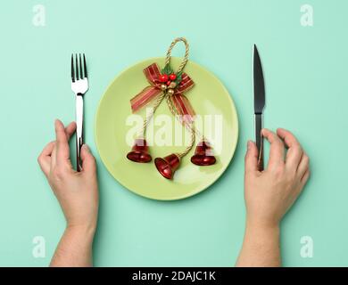 round green ceramic plate, two hands holding a knife and fork on a green background, festive table setting for christmas and new year, top view Stock Photo