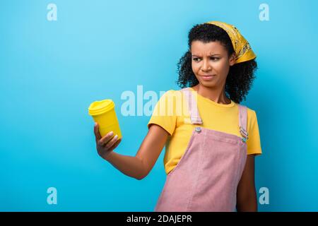 skeptical african american woman holding reusable cup on blue Stock Photo