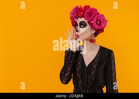 Beautiful girl in halloween makeup and flower wreath screaming aside isolated over yellow wall Stock Photo