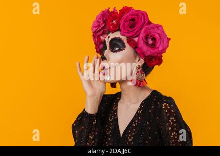 Beautiful girl in halloween makeup and flower wreath screaming aside isolated over yellow wall Stock Photo