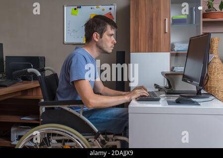 Disabled man is sitting on wheelchair and working in office. Stock Photo