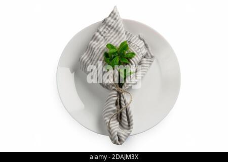One serving napkin with jute rope and ribbon and mint or basil plant laying on clean white table. Setting concept isolated on white background with co Stock Photo