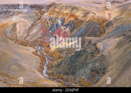 Colorful autumn top view of multi-colored mountains with cracks and rifts, meandering river and golden larch trees Stock Photo