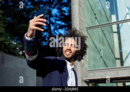 Portrait of smiling afro man taking selfie outside in city Stock Photo