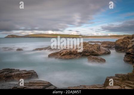 Long exposure looking from the rugged rocky foreshore of Treyarnon point across Constantine bay towards Dinas head on the north cornwall coast. Stock Photo