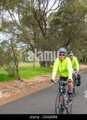 Touring cyclists travelling on vacation riding bicycles on a country road in Margaret River Region Western Australia Stock Photo