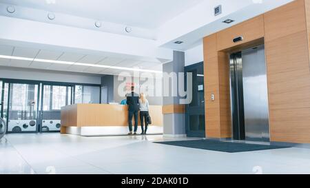 In the Hospital Lobby Young Couple Patients Talks to Receptionist. New, Modern Medical Facility. Stock Photo