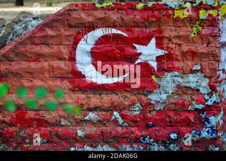 Flag of Turkey painted on old brick wall with blurred green leaves. Nationalism or patriotism concept. Close up angle. Stock Photo