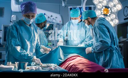 Diverse Team of Professional Surgeons Performing Invasive Surgery on a Patient in the Hospital Operating Room. Nurse Picks Up Instruments Stock Photo