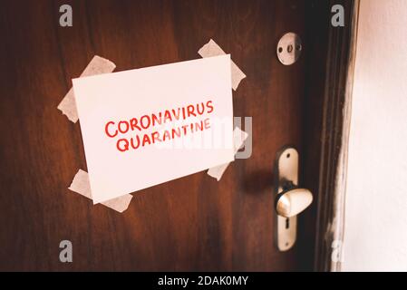 Sheet of Paper With Coronavirus Quarantine Text Hand Written in Red Letters Taped on Wooden Door Next to the Handle and Keyhole Stock Photo