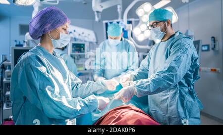 Shot in the Operating Room Assistant Hands out Instruments to Surgeons During Operation. Surgery in Progress. Professional Medical Doctors Performing Stock Photo