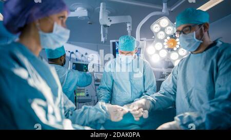 Shot in the Operating Room Assistant Hands out Instruments to Surgeons During Operation. Surgery in Progress. Professional Medical Doctors Performing Stock Photo