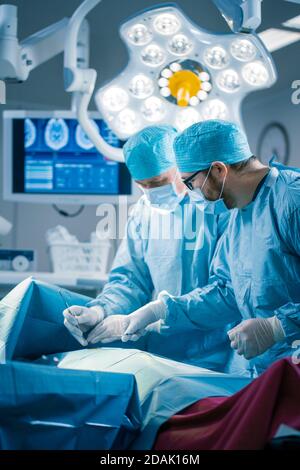 Portrait of the Professional Surgeons Performing Invasive Surgery on a Patient in the Hospital Operating Room. In the Background Modern Hospital Stock Photo