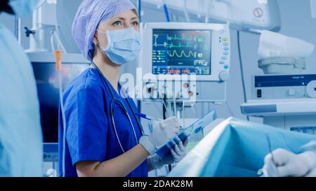 In the Hospital Operating Room Anesthesiologist Looks and Monitors and Controls Patient's Vital Signs, Nodding to a Chief Surgeon to Proceed with Stock Photo