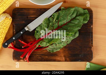 Bunch of beet leaves on wooden cutting board and knife on table Stock Photo