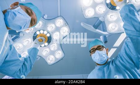 Low Angle Shot POV Patient View: Two Professional Surgeons Turning on Surgery Lights while Bending over Patient. Stock Photo
