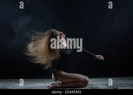 A long-haired girl in a black bodysuit in flour in a black studio. Stock Photo