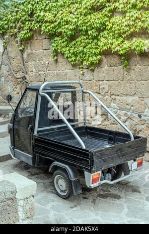 three-wheeler parked near green creeper on stone wall at historical hilltop village, shot in bright light at Civita di Bagnoregio, Viterbo, Lazio, Ita Stock Photo