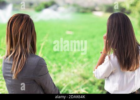 Two business women in front of a field with agriculture irrigation system. Water sprinklers in the background. Stock Photo