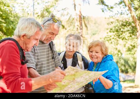 Group of active seniors with hiking map looking for direction in nature in summer