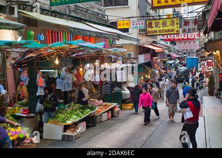 A fruit and vegetable stall at a narrow back street market in central Hong Kong with people walking through and looking at what is for sale Stock Photo