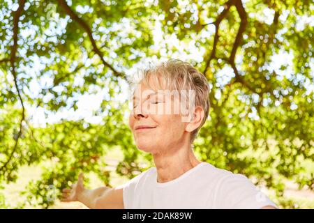 Senior woman with closed eyes doing a breathing exercise and meditation in nature Stock Photo