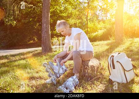 Elderly woman inline skating puts on inline skates in the summer in nature Stock Photo