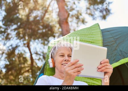 Senior woman using tablet computer and headphones in front of tent while listening to music Stock Photo