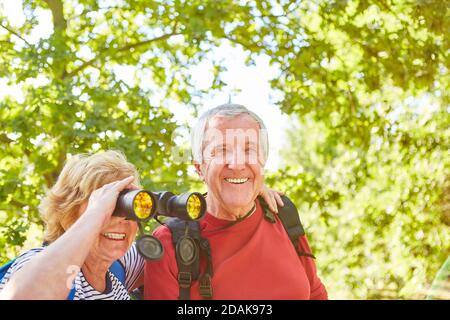 Happy active senior couple as ornithologists with binoculars while bird watching Stock Photo
