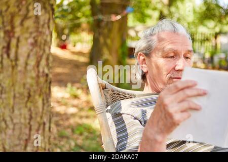 Smiling senior retired man reading book while relaxing in garden Stock Photo