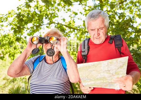 Active senior couple as ornithologists with binoculars and map in summer in the forest Stock Photo