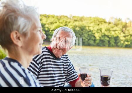 Senior couple drinking a glass of red wine together at the lake and celebrating an anniversary Stock Photo