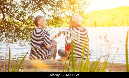 Elderly couple of seniors drinking red wine on the shore of the lake in summer Stock Photo