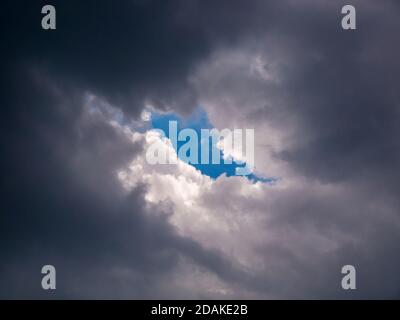 A piece of blue sky in a hole in the thick rain clouds Stock Photo