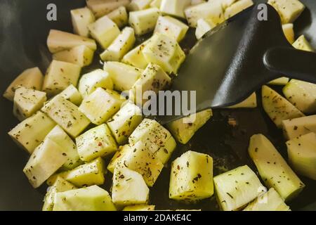 Vegetable squash in square pieces are fried in a pan. Zucchini pieces cooking with herbal spices Stock Photo