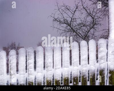 The tips of the fence covered with snow creates a contrast to the dark washed sky with a snowstorm - snowfall caught in motion Stock Photo