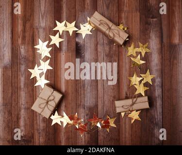 Party Mock Up with Round Gold Stars Frame on Dark Wood Background. Christmas Shiny Golden Tinsel and Gifts. Card Design with Copy Space for Text Stock Photo