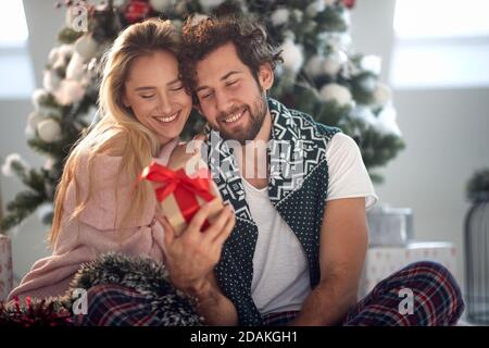 beardy caucasian guy looking with smile wrapped present holding in hand with beautiful blonde leaned on his shoulder Stock Photo