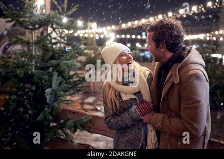 A young happy couple enjoying snowfall in a magical night in the city. Christmas tree, love, relationship, Xmas, snow Stock Photo